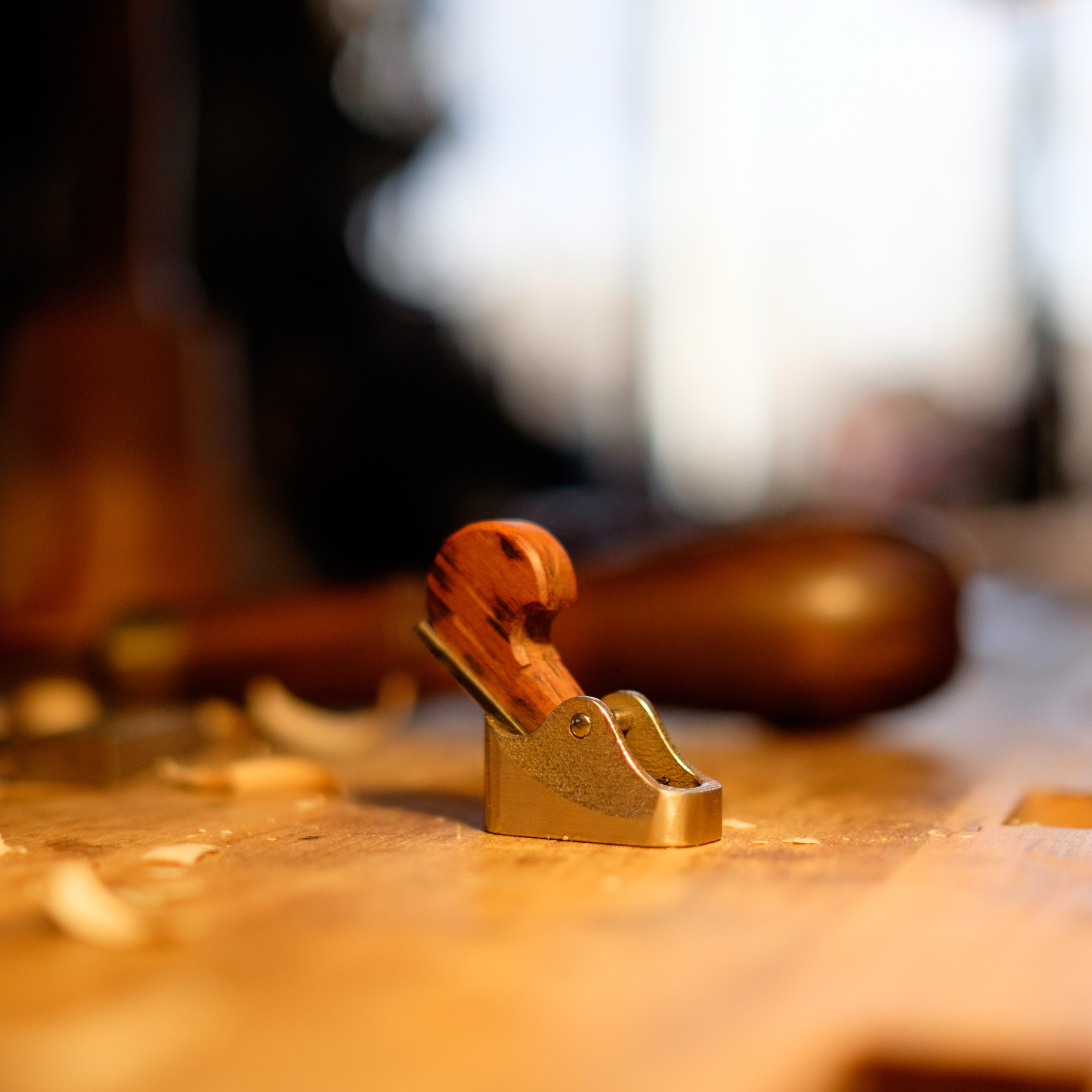 Solid brass luthier finger plane with curly wood shaving on workbench